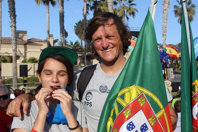 Foto da Marta, j medalhada, acompanhada pelo seu treinador, que segura a bandeira de Portugal
