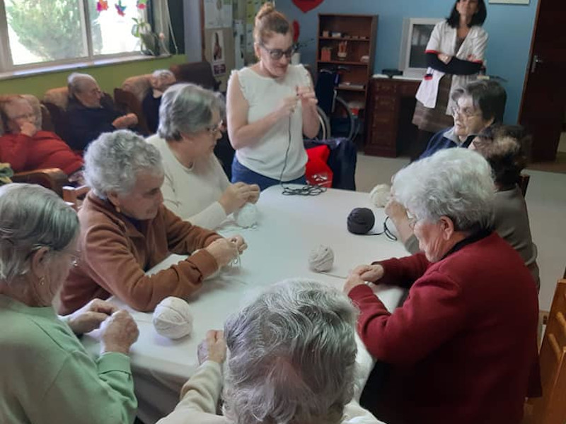 Dinamizadora da ação e idosos participantes em torno de uma mesa, manipulando os materiais utilizados.