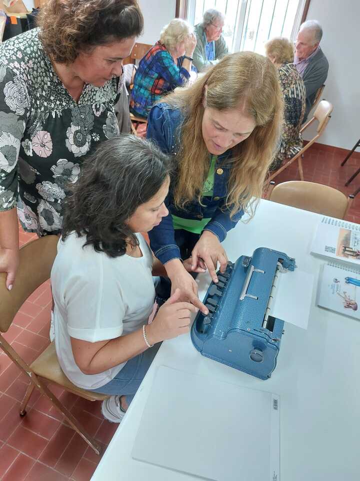 Três pessoas em volta de uma mesa com uma máquina Braille