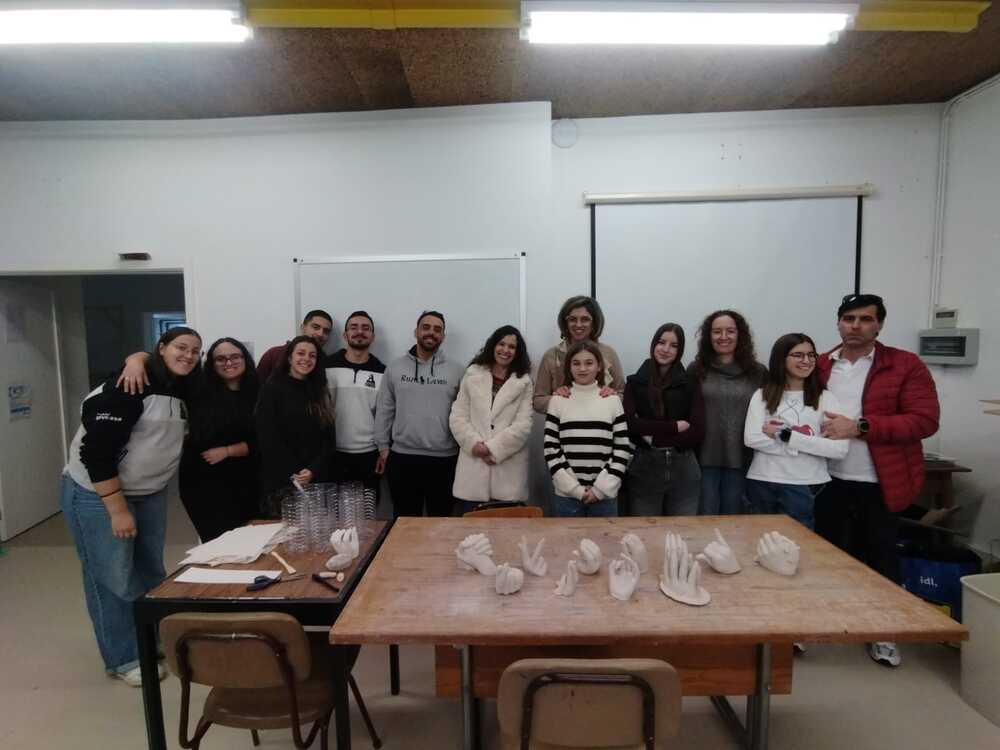 Foto de grupo com alunos e participantes na atividade atrás de uma mesa em que se vêem vários moldes de mãos